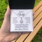 Hand holding the open To My Wife necklace gift box outdoors on a park bench