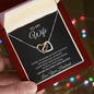 Hand holding the To My Wife necklace gift box in front of warm holiday lights